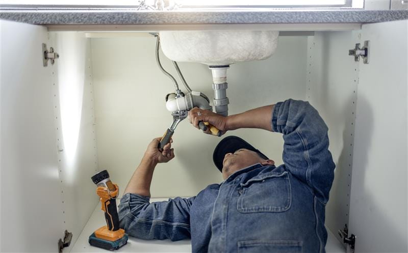 Plumber repairing pipes beneath a bathroom sink in Glendale